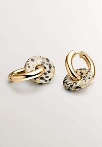 Pendientes de aro en tono dorado con un acento de disco de piedra moteada. El diseño incluye curvas suaves y una combinación de materiales.
