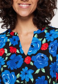 Svart tygklänning med blommönster av stora blå och röda blommor. V-ringad design med gröna bladdetaljer. Mjuk textur.