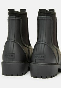 Fekete gumírból készült Chelsea csizma elasztikus panelek, textúrázott felső felület és mély barázdázott talp jellemzi. A saroknál kiemelkedő logó található.