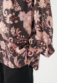 Blusa scura floreale con intricati motivi paisley e floreali in tonalità di rosa e arancione. Tessuto morbido con dettagli sulle maniche arricciate.
