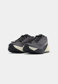 Chaussures de course noires avec un dessus texturé, des lacets plats et une semelle intermédiaire en mousse blanche. Motif de traction robuste sur la semelle extérieure en caoutchouc.