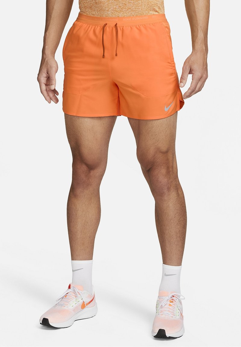 Oranssit Nike-juoksushortsit, joissa on joustava vyötärö, nyöri ja pieni logoaksentti. Sujuva kangas ja polven yläpuolelle ulottuva leikkaus.