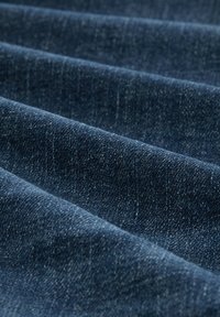 Țesătură din denim de culoare albastru închis, cu o suprafață texturată, având un ușor luciu. Plisată și stratificată, evidențiind un model de țesătură consistent.