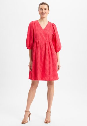 Coral puff-sleeve dress with a V-neck, textured floral pattern, and a gathered waist. Worn with nude sandals against a white background.