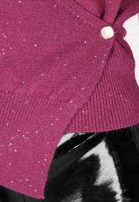 Maglione lavorato a maglia fucsia con paillettes lucenti, dotato di chiusura laterale con bottoni. La texture è morbida, con orlo a coste e caduta giocosa.