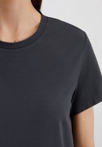 T-shirt in cotone grigio scuro con scollo rotondo classico e maniche corte. Il tessuto ha una texture liscia con una leggera lucentezza.