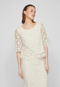 Hvit heklet topp med blomsterdesign og korte ermer, med rund halslinning og lagdelt design.