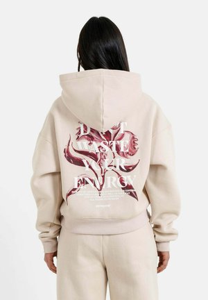 Hoodie beige avec un grand graphique en texte rouge et blanc au dos. Doté d'une capuche et de poignets côtelés, fabriqué en matériau doux.