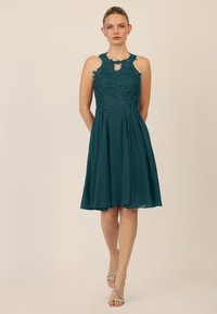 Turquoise mouwloze jurk met kant bodice, keyhole halslijn en zwierige rok. Bevat ingewikkelde floral borduursels en een uitlopende silhouet.