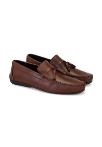 Bruine leren moccasinschoenen met een gestikt ontwerp, platte zool en kwastaccenten; gladde textuur en ronde neusvorm.