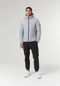 Világosszürke bélelt dzseki cipzáras záródással, kapucnival és két oldalzsebbel. Fekete cargo nadrággal és fehér tornacipővel párosítva.