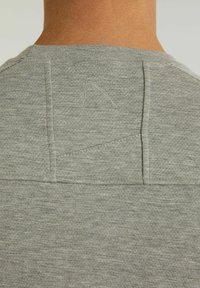 Grau T-Shirt aus einem strukturierten, weichen Stoff mit einem kleinen Logo, das auf dem hinteren Nacken gestickt ist. Gerundeter Halsausschnitt und verstärkte Nähte.