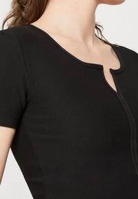 Top noir à côtes avec des manches courtes, présentant un col arrondi et un détail en forme de trou de serrure à l'avant. Texture lisse et coupe ajustée.