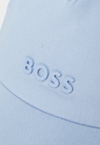 Lyseblå caps laget av teksturert stoff med en hevet, tykk logo "BOSS" i matchende farge på forsiden.