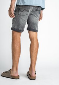 Grå denimshorts med uppvikta fållar, med bakfickor och subtila blekningar. Matchas med bruna slip-on sandaler.