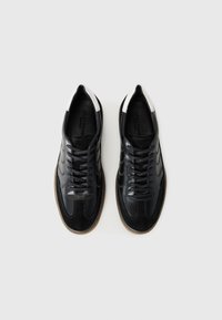 Melnas ādas sporta kurpes ar kontrastējošu baltu papēdi, apaļu purngalu un šņorēšanas sistēmu. Iespējas šūtu detalizāciju un teksturētu zoli.