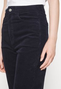 Navy corduroy jeans with a high waist, featuring a front pocket, subtle texture, and a silver button closure at the waistband.