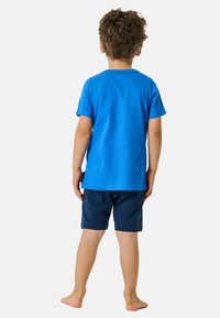 T-shirt in cotone blu con maniche corte abbinato a pantaloni corti blu scuro, visto da dietro. Presenta un orlo dritto e una vestibilità casual.