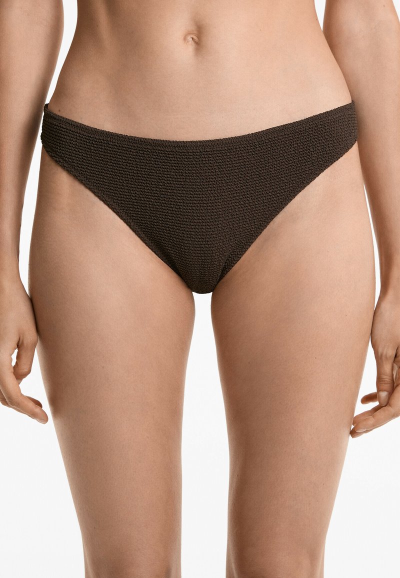 Barna bikini alsó, amely texturált anyagból készült, alacsony derékkal rendelkezik, és mérsékelt fedést biztosít az oldalakon. Egyszerű és varrás nélküli szélek.
