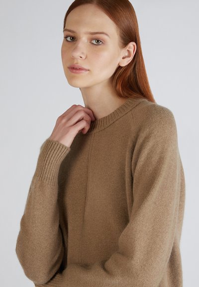 Maglione a maglia beige con scollatura tonda, polsini a costine e una consistenza morbida. Il tessuto appare caldo e confortevole con una leggera lucentezza.