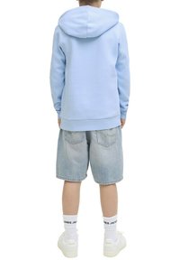 Un sweat à capuche bleu clair, associé à un short en denim clair. Des baskets blanches et des chaussettes blanches avec une marque visible au-dessus du talon.