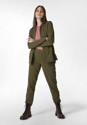 Olivově zelený blazer a odpovídající kalhoty s růžovým topem, který má minimalistický design. Modelka má na sobě bordó šněrovací boty.