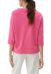 Rosa bomullströja med 3/4-ärmar, en lös passform och rundad halsringning. Slät textur och enkla sömnadsdetaljer. Bärs med vita byxor.