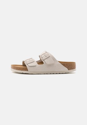 Infradito in suede beige con due fibbie regolabili, soletta in sughero e suola in gomma, caratterizzati da una leggera curvatura del tacco.