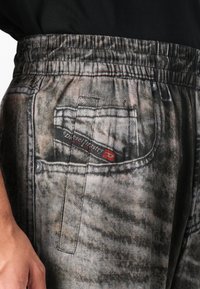 Grijze denim joggers met een elastische tailleband, voorzien van een achterzak, bedrukt textuur en een merkteken in het rood op de zak.