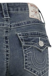 Temno modri kavbojke z več žepi, belimi šivi in blagovno znamko na pasu. Zadnji žep ima edinstveno zasnovo.