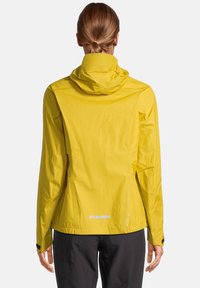 Gele waterdichte jas met capuchon, gladde textuur, elastische manchetten en reflecterende accenten op de taille en rug voor zichtbaarheid.