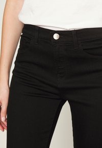 Svarta denimjeans med midjehög passform, med silvrig knappstängning, fem fickor och en slät textur.