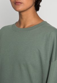 Felpa a girocollo in cotone verde oliva con una vestibilità rilassata. Presenta un collo a costine e una texture morbida e liscia. Nessun motivo o accento visibile.
