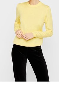 Gul, långärmad stickad topp med rund halsringning. Mjuk textur, figurnära passform, kombinerad med svarta cordpants.