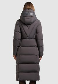 Dlouhý šedý péřový kabát s kapucí, na zadní straně se znakem, prošívaný design a boční zipy. Hladký materiál a délka po kolena.