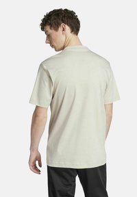 Camiseta de manga corta de color beige claro, hecha de una tela suave, con cuello redondo y un corte relajado. La vista posterior muestra una textura lisa y un diseño sencillo.