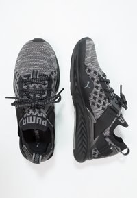 Chaussures de sport grises et noires avec une tige en tricot texturé, un laçage sécurisé, et des semelles en caoutchouc présentant un motif en zigzag ainsi que le logo Puma.