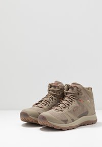 Stivali da trekking beige con design alto, parte superiore in rete, suola in gomma e accenti grigi a contrasto. Presentano lacci e un colletto imbottito.