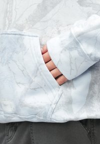 Világoskék kapucnis pulóver puha tapintással, finom levélmintával és elülső erszénnyel. Mandzsettás ujjak és lekerekített alsó szegély.