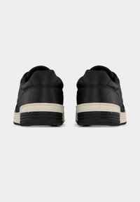 Ζευγάρι μαύρα παπούτσια χαμηλού ύψους με λευκές μεσαίες σόλες και μαύρες εξωτερικές σόλες, εμφανιζόμενα από την πίσω πλευρά σε απλό φωτεινό φόντο.