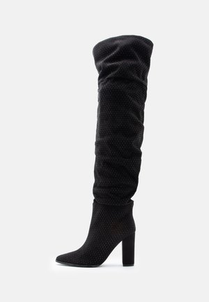 Over-the-knee black boot in soft fabric with gathered texture, pointed toe, and chunky heel, featuring a subtle dotted pattern throughout.
