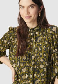 Zielona bluzka w panterkę z wysokim falbaniastym dekoltem i bufkami. Miękka tkanina o swobodnym kroju, z beżowymi i czarnymi plamkami.