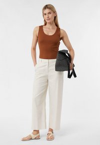 Brązowy, prążkowany top na ramiączkach, kremowe spodnie typu wide-leg i beżowe sandały. Torebka w czarno-białe paski z kokardą. Prosty, nowoczesny design.