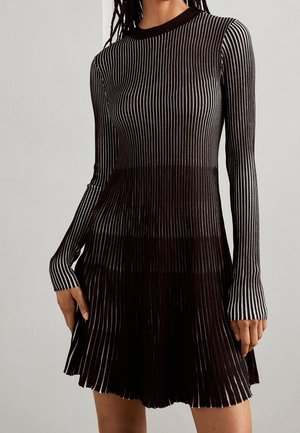 Woman wearing a black and white vertical striped long-sleeve dress with a fitted bodice and flared skirt.