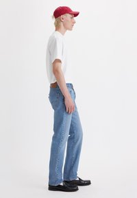 White short-sleeve t-shirt, light blue jeans, and black shoes. The cap is red. The design is casual with a straight-fit silhouette.