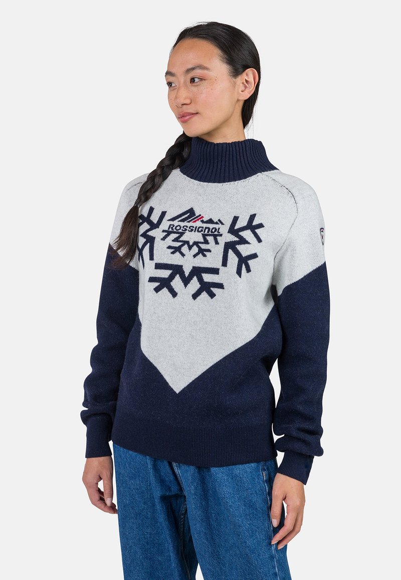 Marineblauer und hellgrauer Wollpullover mit hohem Kragen, der mit Schneeflockenmuster und einem Logo auf der Brust versehen ist. Gerippte Bündchen und Saum.