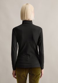 Musta pitkähihainen poolopaita, jossa on slim fit -mitoitus, sileä pinta ja minimalisti yksityiskohdat, yhdistettynä oliivinvihreisiin farkkuihin.