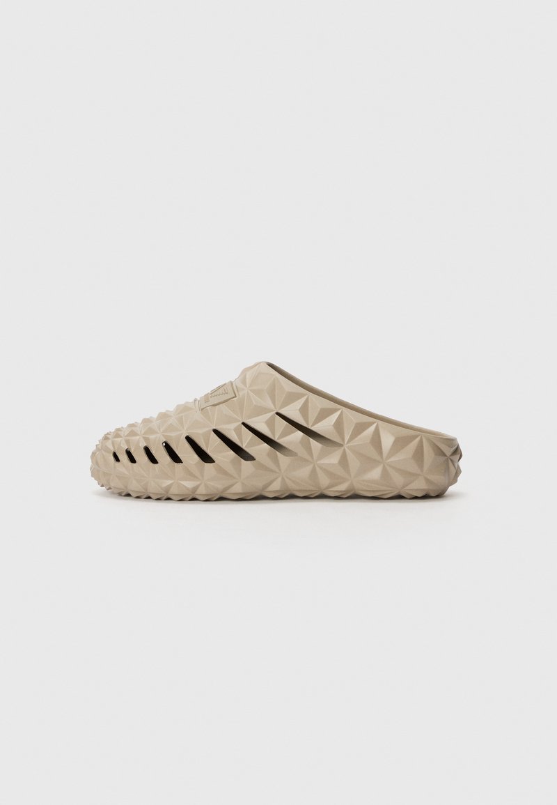 Beige gummistøvler med et teksturert pyramidemønster og sideåpninger for ventilasjon, med rund tå og flat, formet såle.
