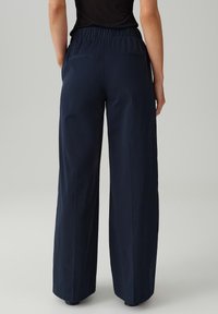 Marineblauwe wijde broek met een elastische tailleband, uitgerust met achterzakken en een gladde textuur, ontworpen voor een ontspannen pasvorm.