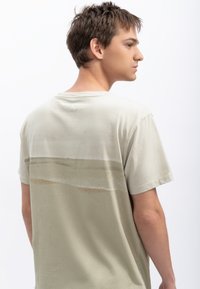 Lichtgroen katoenen t-shirt met korte mouwen, voorzien van een horizontaal verfsstrookontwerp in beige op de rug nabij de schouders.